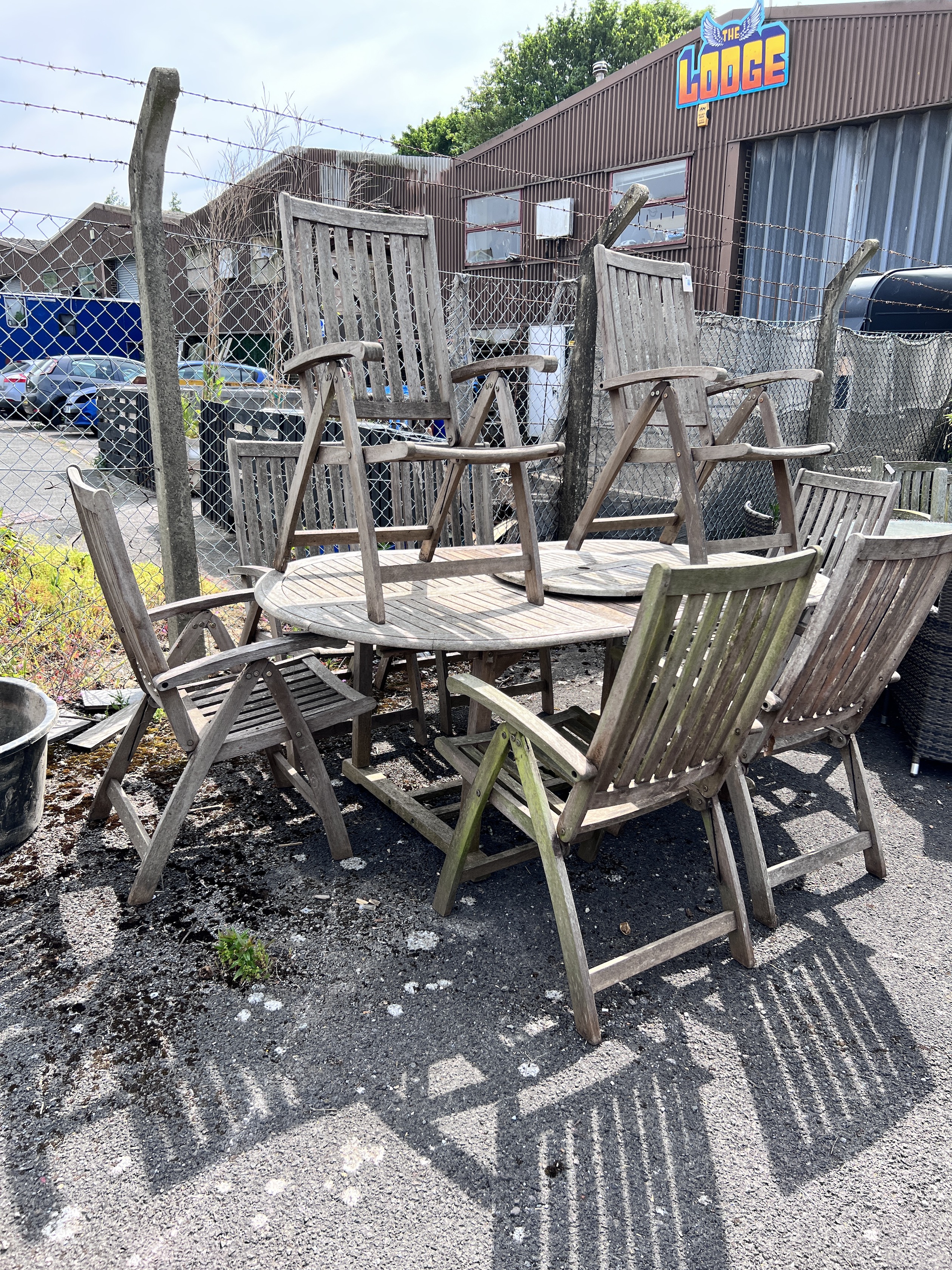 A weathered teak oval extending dining table and eight folding elbow chairs (7 plus 1), table 208cm extended, depth 110cm, height 76cm